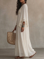 Lifestyle shot of a woman walking on a beach at sunset, showcasing the ethereal drape of the ivory batwing dress.